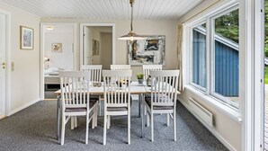 A dining area with a white table and chairs, a hanging light fixture, and a large window with a view of greenery.