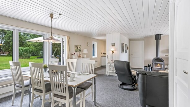 A modern kitchen with a built-in stove, a dining area with white chairs and a table, and a view of a garden through large windows.