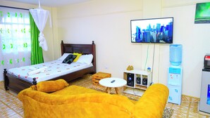 Et hotelværelse med seng, sofa, fjernsyn, vanddispenser og et lille bord.