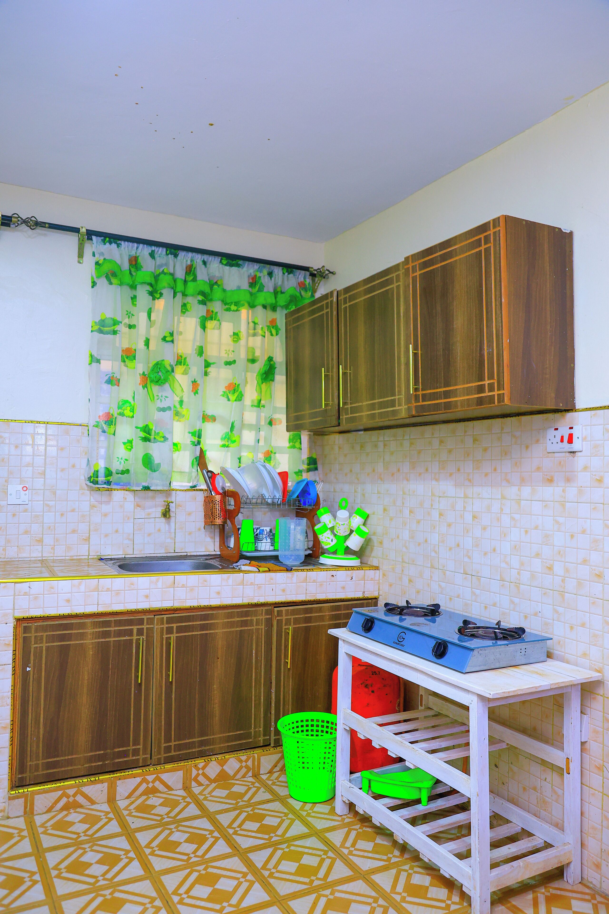 Cozinha com armários de madeira, fogão a gás, pia e piso revestido de azulejos.