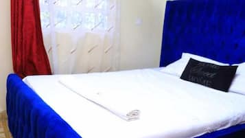 Een bed met een blauw hoofdeinde, witte beddengoed, een rood gordijn en een wit muggengaas.