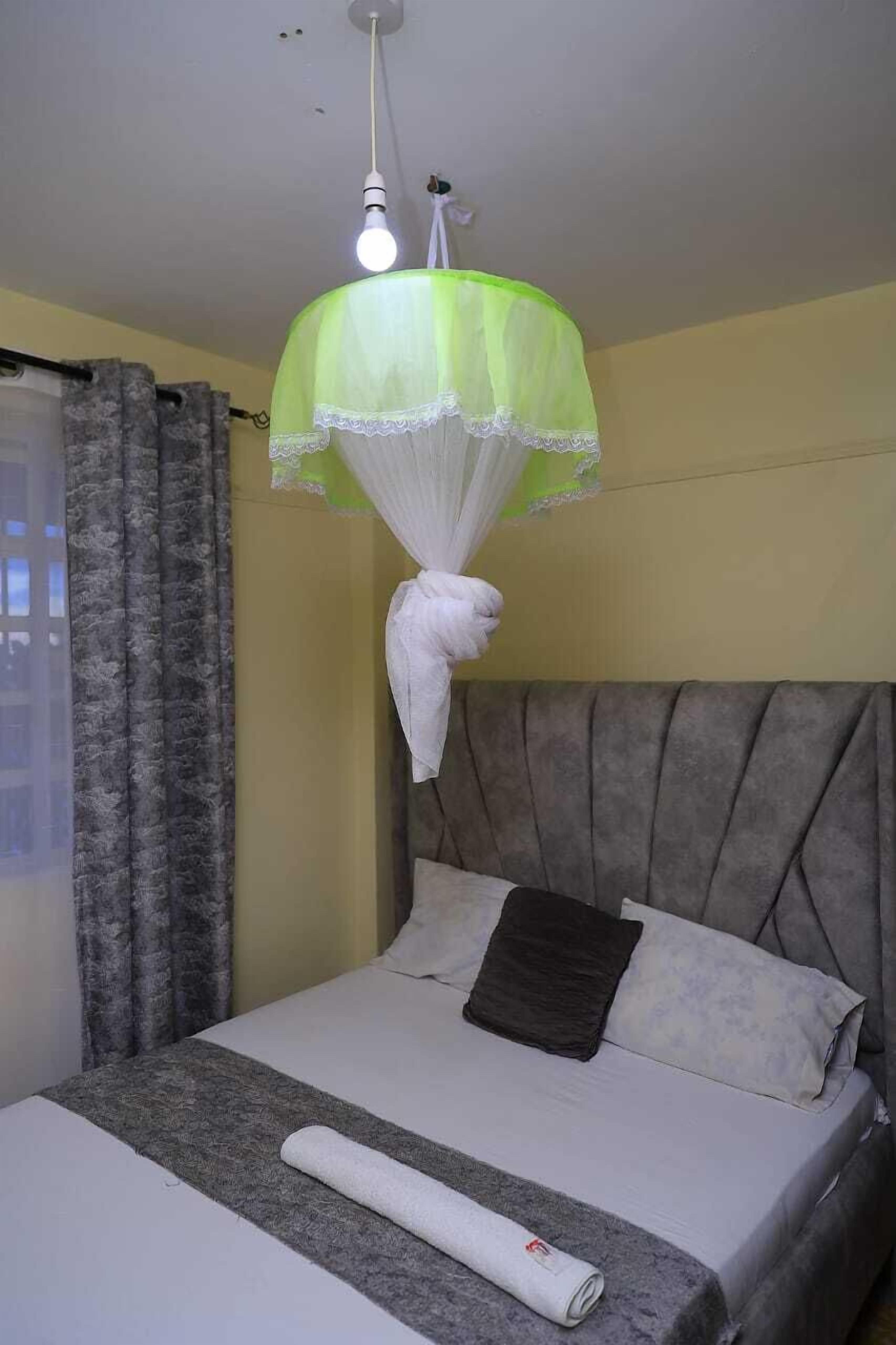 A neatly made bed with a grey headboard, a white pillow, and a rolled white towel.