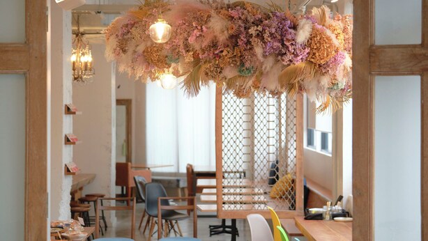 Un comedor con mesas y sillas de madera, un arreglo floral colgante y una pared decorativa con diseño de celosía.