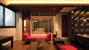 Una habitación de hotel moderna con un sofá rojo, una mesa de centro de madera y un comedor con mesa y sillas.