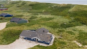 A coastal property with a main house and several smaller buildings, surrounded by grassy dunes and a view of the sea.