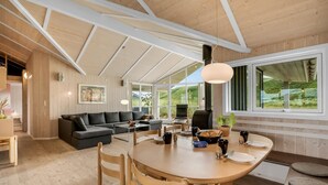 A modern interior with a high ceiling, wooden beams, a round dining table, and a cozy seating area.