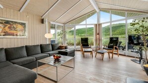 A modern living room with a large sofa, a coffee table, and a TV area with chairs and a grill.