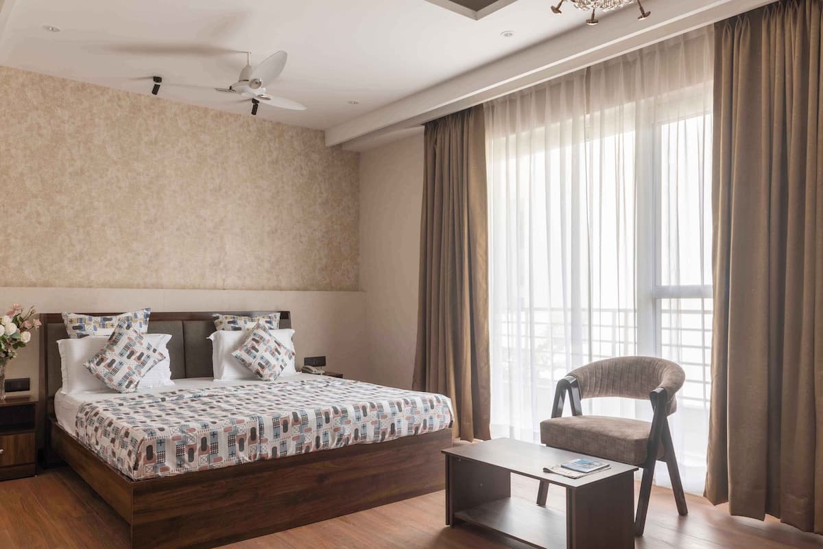 A modern bedroom with a large bed, a wooden nightstand, a chair, a small table, and a ceiling fan.