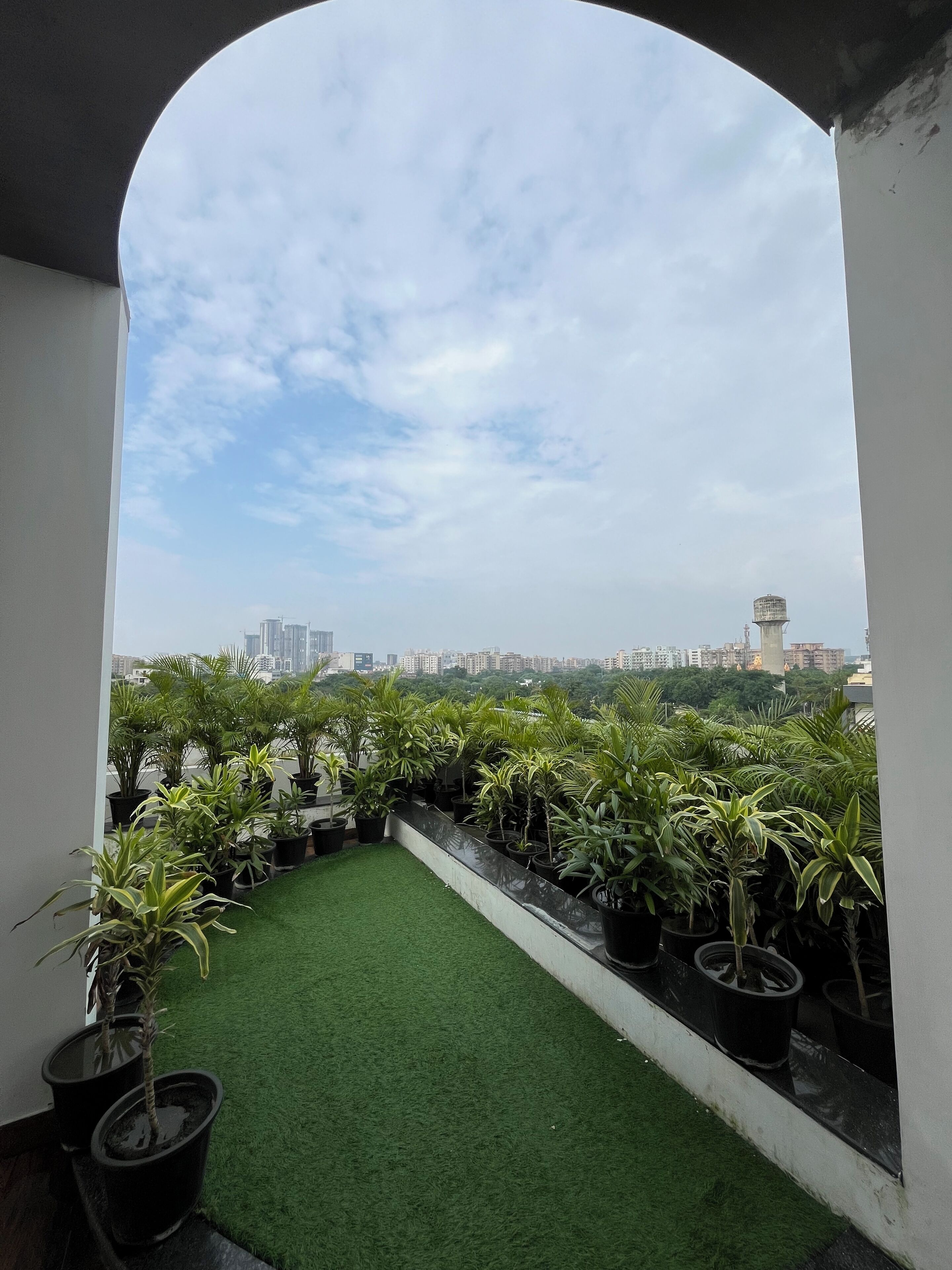 A rooftop terrace with artificial grass and potted plants, offering a view of the city skyline.
