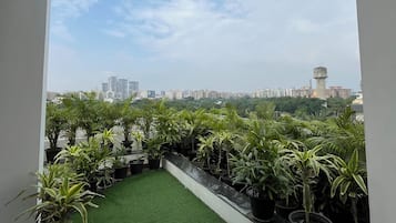 A rooftop terrace with artificial grass and potted plants, offering a view of the city skyline.