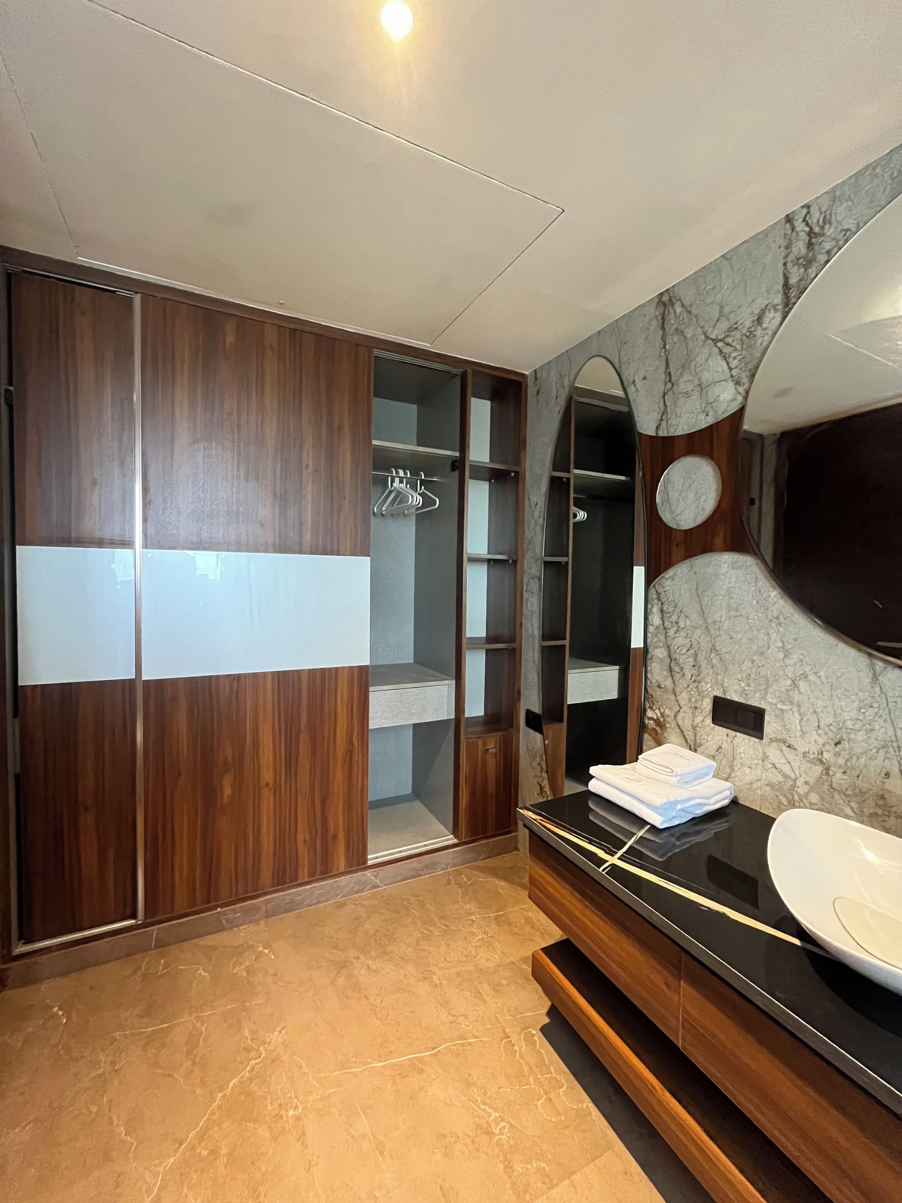 A modern bathroom with a wooden vanity, a large mirror, and a marble backsplash.