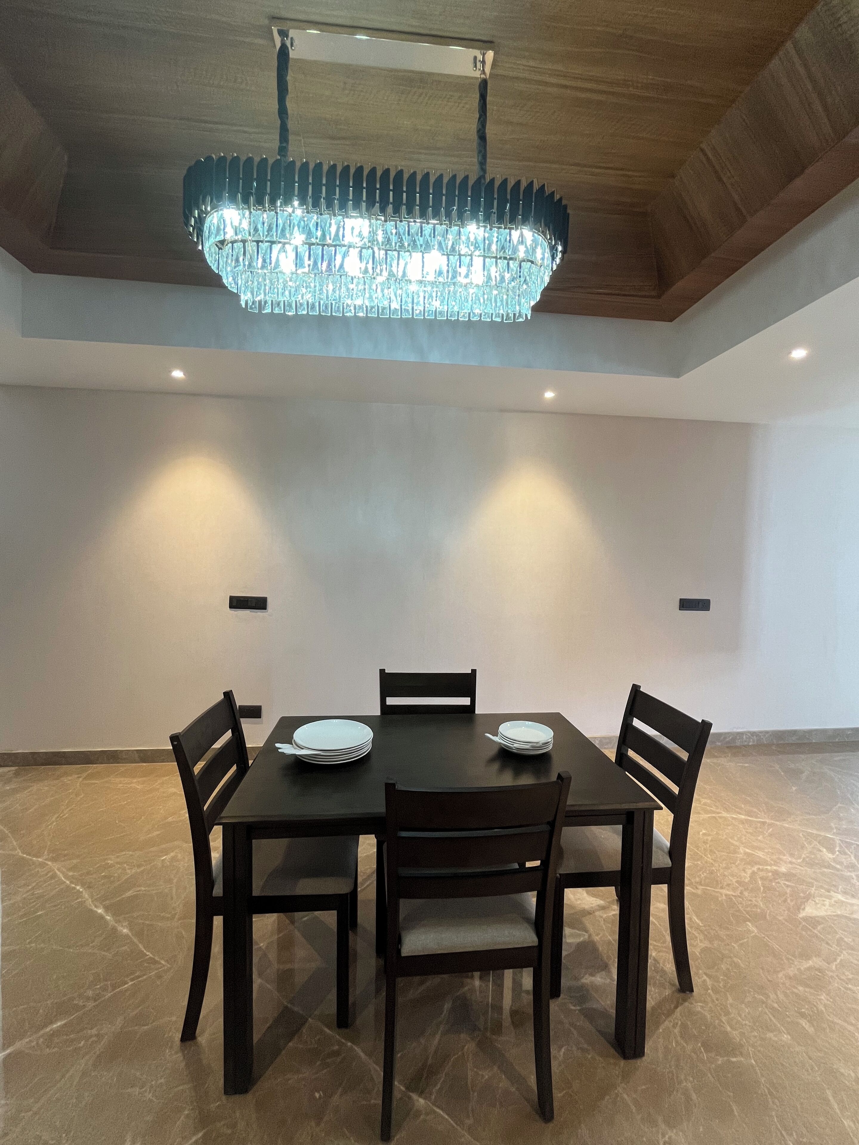 Un comedor con una mesa de madera oscura, cuatro sillas y una gran lámpara de cristal.
