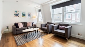 A modern living room with a grey sofa set, a coffee table, and a large window with blinds. - Stylish 2BR 2BA by the Heart of Soho (London)