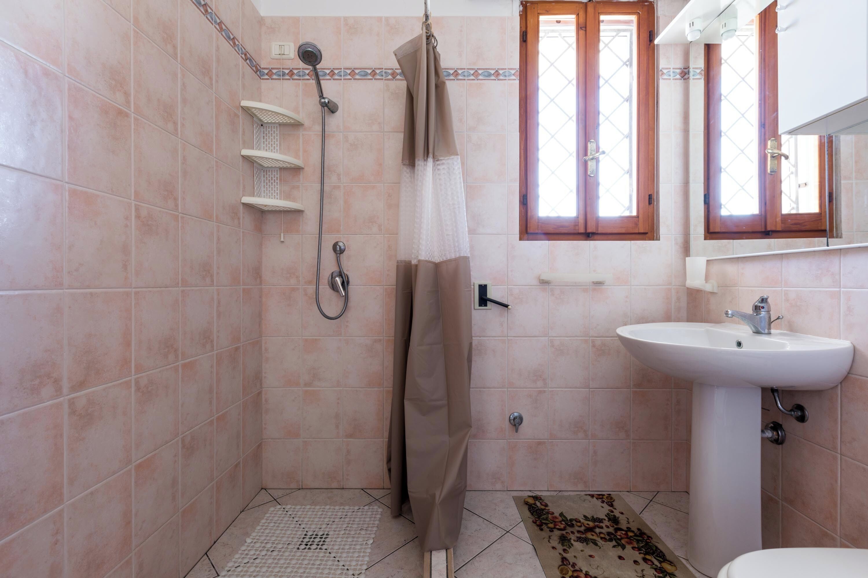 Un baño con ducha, lavamanos y una ventana con cortinas.