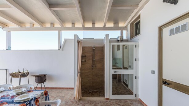 A room with a dining table set for four, a small grill, and a shower area. - 4174 Villetta Olmo by Barbarhouse (Porto Cesareo)