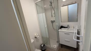 Un baño moderno con ducha envuelta en vidrio, inodoro blanco y tocador con espejo.