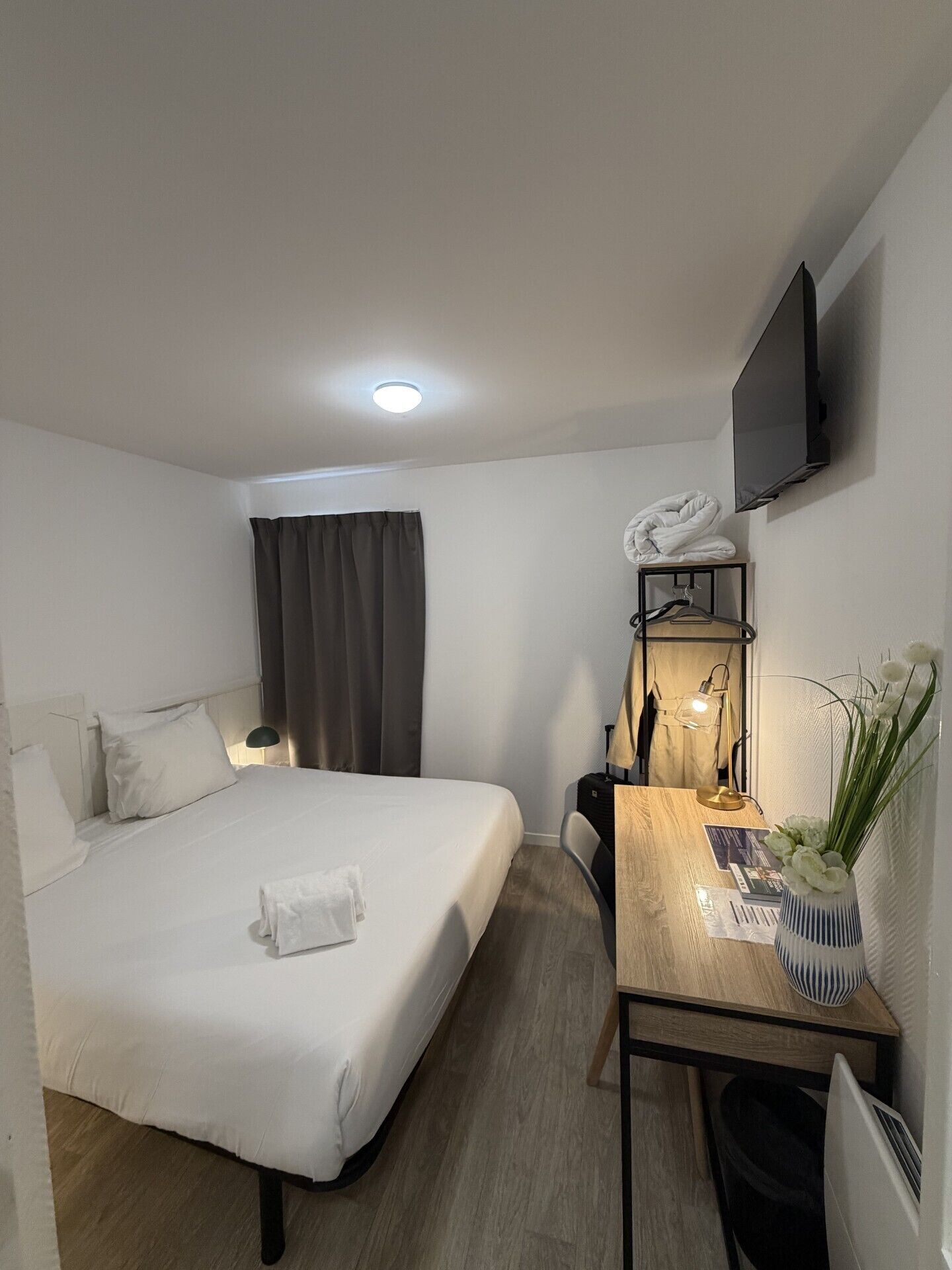 Hotelkamer met een bed, bureau, stoel, televisie aan de wand en een raam met gordijnen.