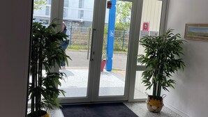 A hotel entrance with a glass door, potted plants, a blue pillar, and a framed picture on the wall. - Parc Hotel (Carrieres-sous-Poissy)