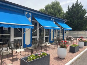 An outdoor seating area with blue awnings, outdoor tables, and chairs, and potted plants. - Parc Hotel (Carrieres-sous-Poissy)