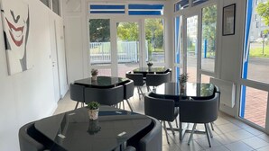A modern indoor space with multiple round tables and chairs, large windows with blue frames, and a tiled floor. - Parc Hotel (Carrieres-sous-Poissy)