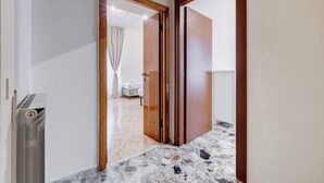 A hallway with a tiled floor leading to a bedroom with a bed and a nightstand.