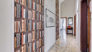A hallway with a bookshelf filled with books, a framed picture on the wall, and a tiled floor.