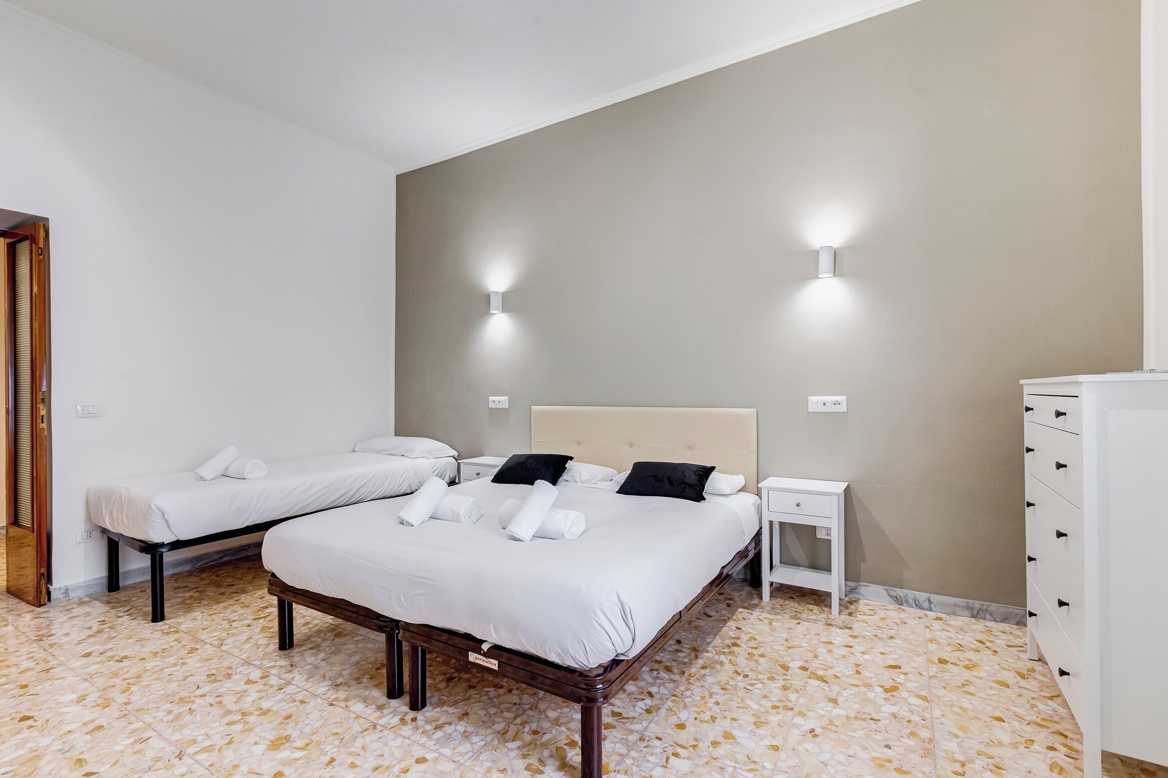 A hotel room with two beds, a nightstand, a dresser, and wall-mounted lights.