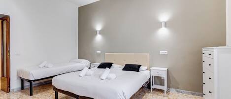 A hotel room with two beds, a nightstand, a dresser, and wall-mounted lights.