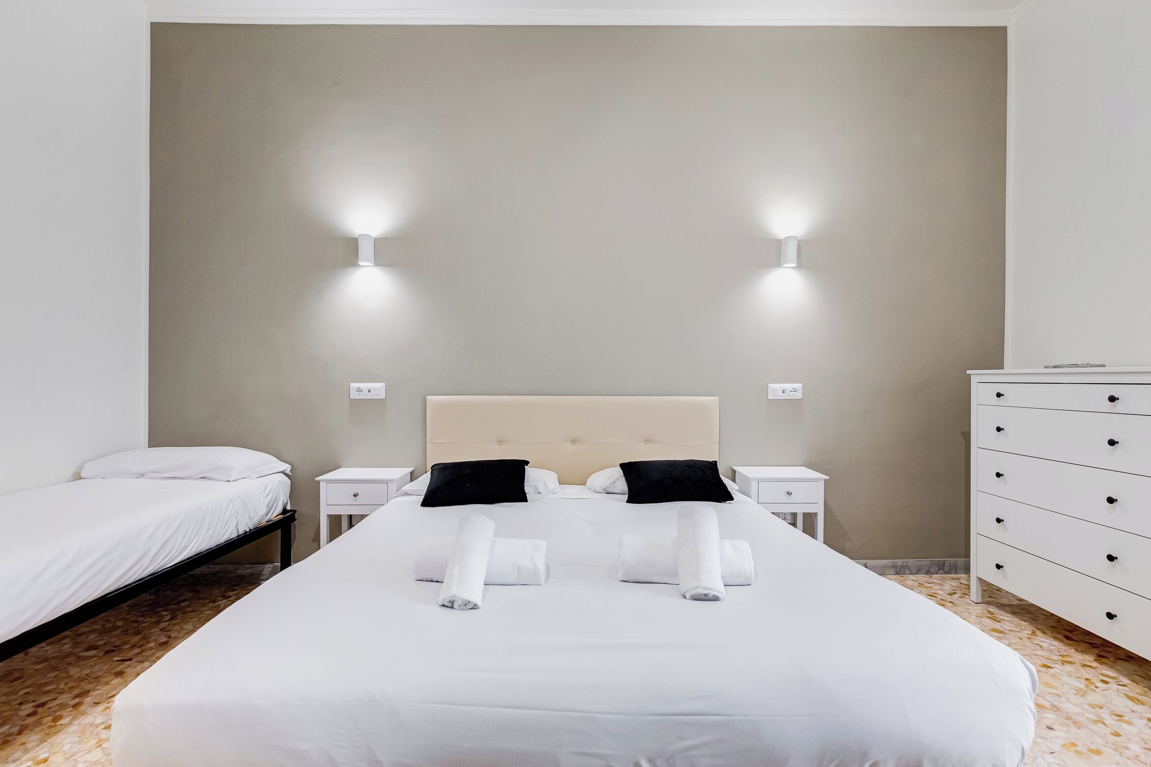 A hotel room with a large bed, two bedside tables, a dresser, and wall-mounted lights.