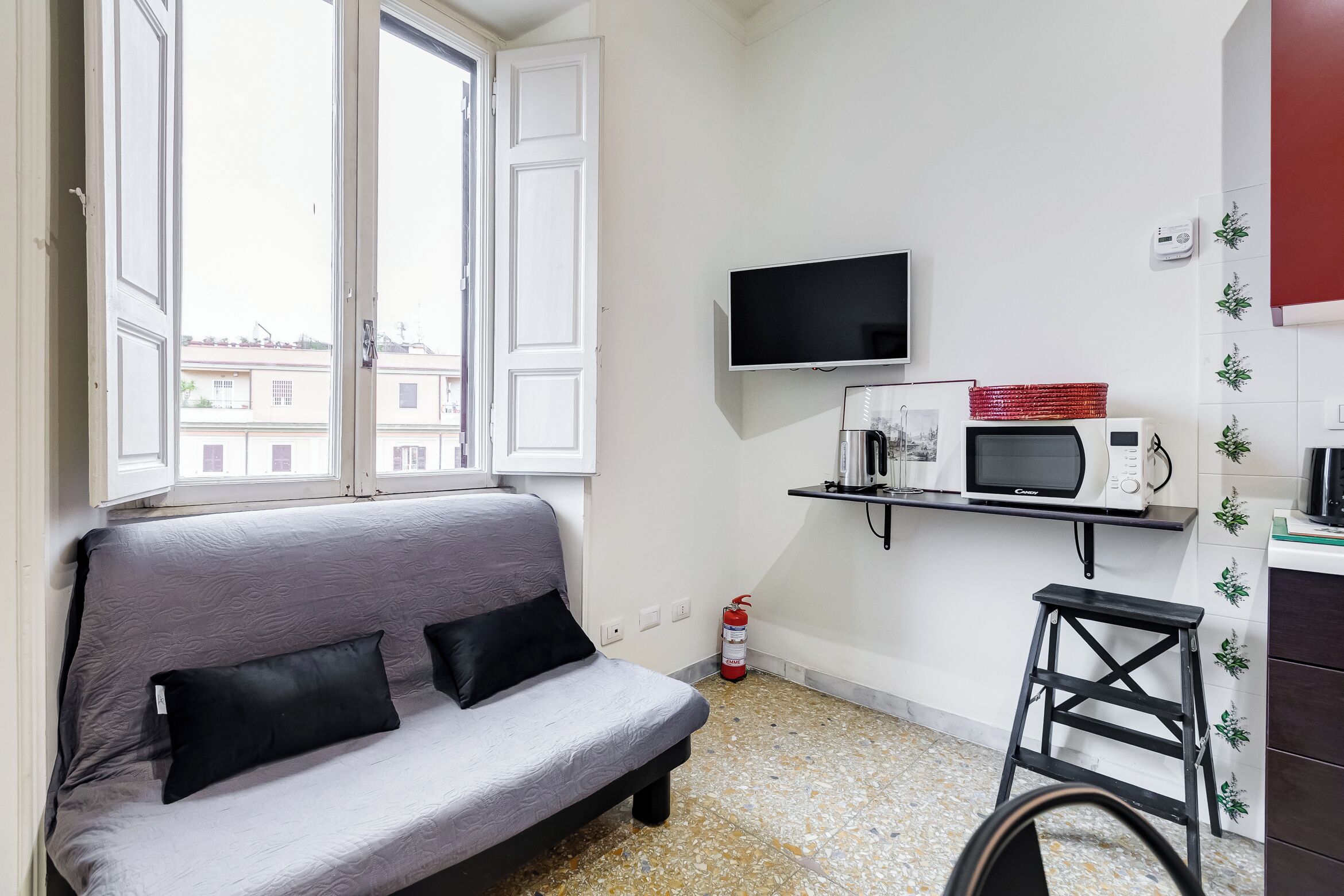 Une petite pièce moderne, équipée d’un canapé, d’une télévision, d’un four à micro-ondes et d’un petit tabouret.