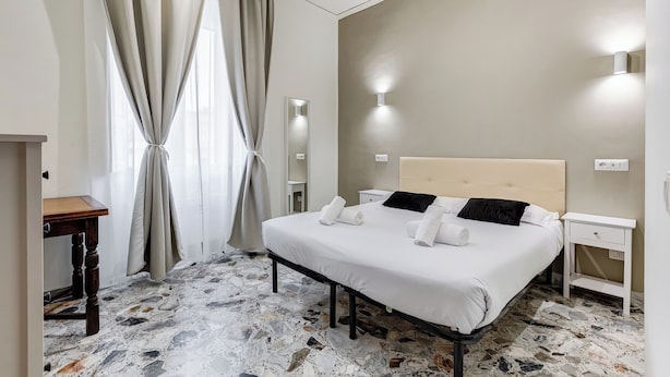 A hotel room with a bed, bedside tables, a mirror, and a wall-mounted light fixture.