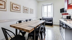 A dining area with a wooden table and black chairs, a kitchen with modern appliances, and framed fish artwork on the wall.