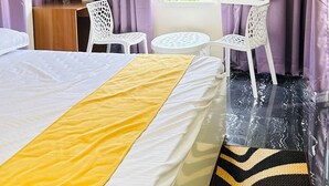 Una habitación de hotel con cama, escritorio con silla, una mesita redonda, televisor y ventana con cortinas.