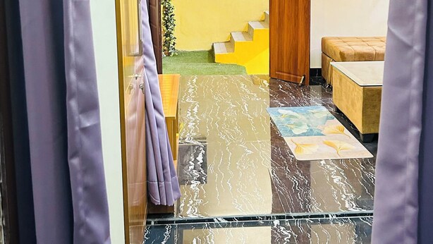 Habitación de hotel con suelo de mármol, puerta de madera, un pequeño sofá, un televisor en la pared y una escalera que lleva a un balcón.