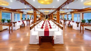 Un salón de banquetes con mesas largas, vigas de madera y ventanas amplias.