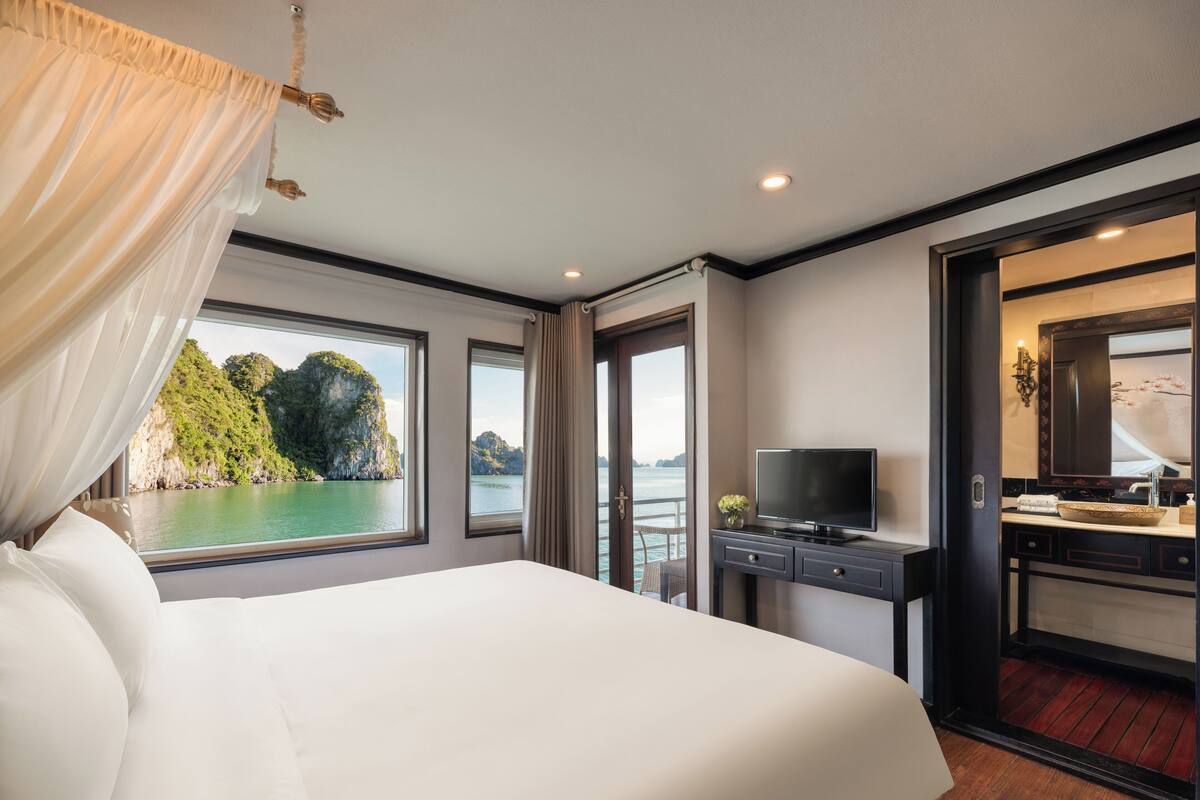 A hotel room with a large bed, a TV, a desk with a computer, and a bathroom with a mirror and sink.