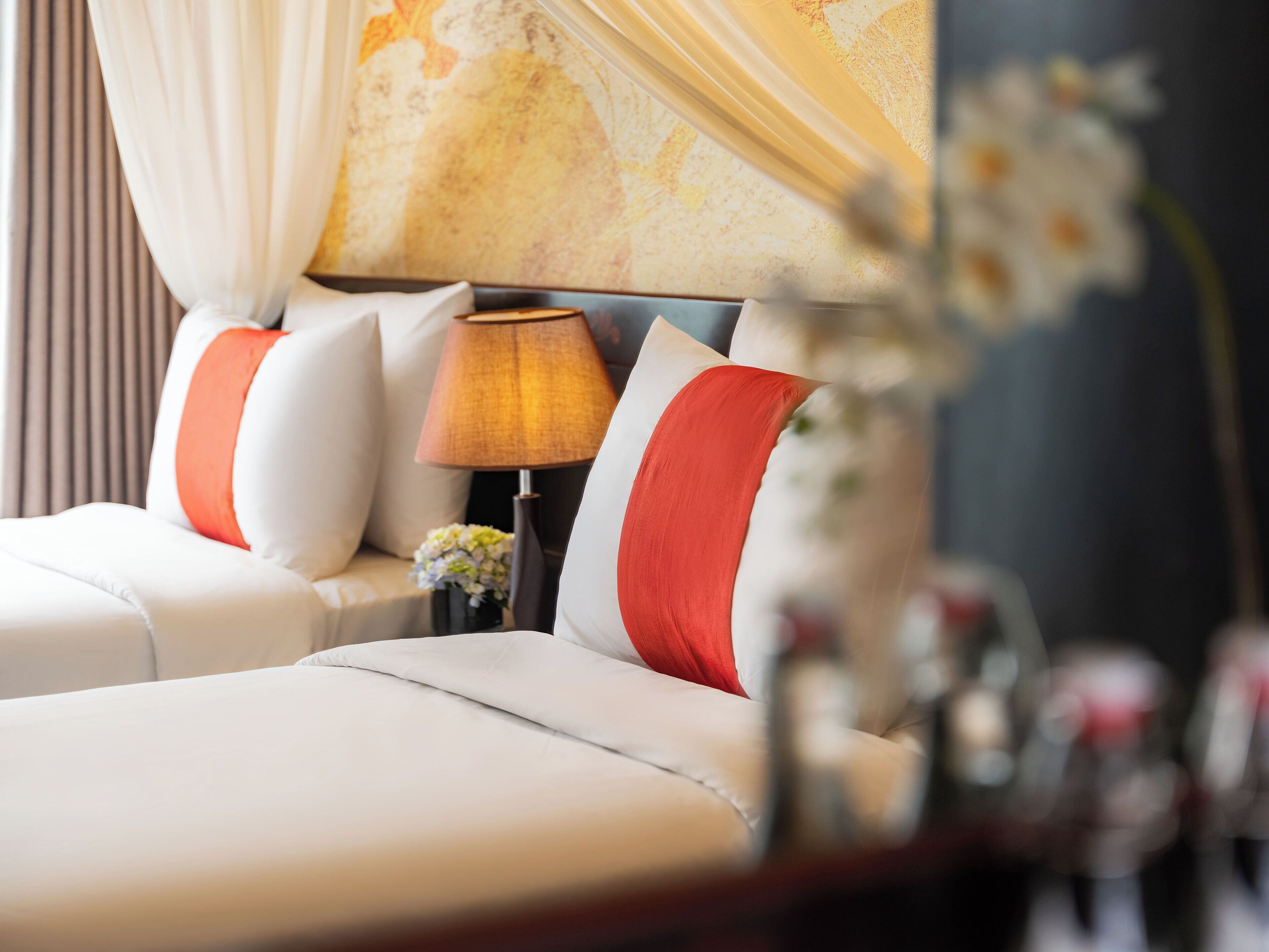 A hotel room with a bed, a nightstand with a lamp, and a vase with flowers.