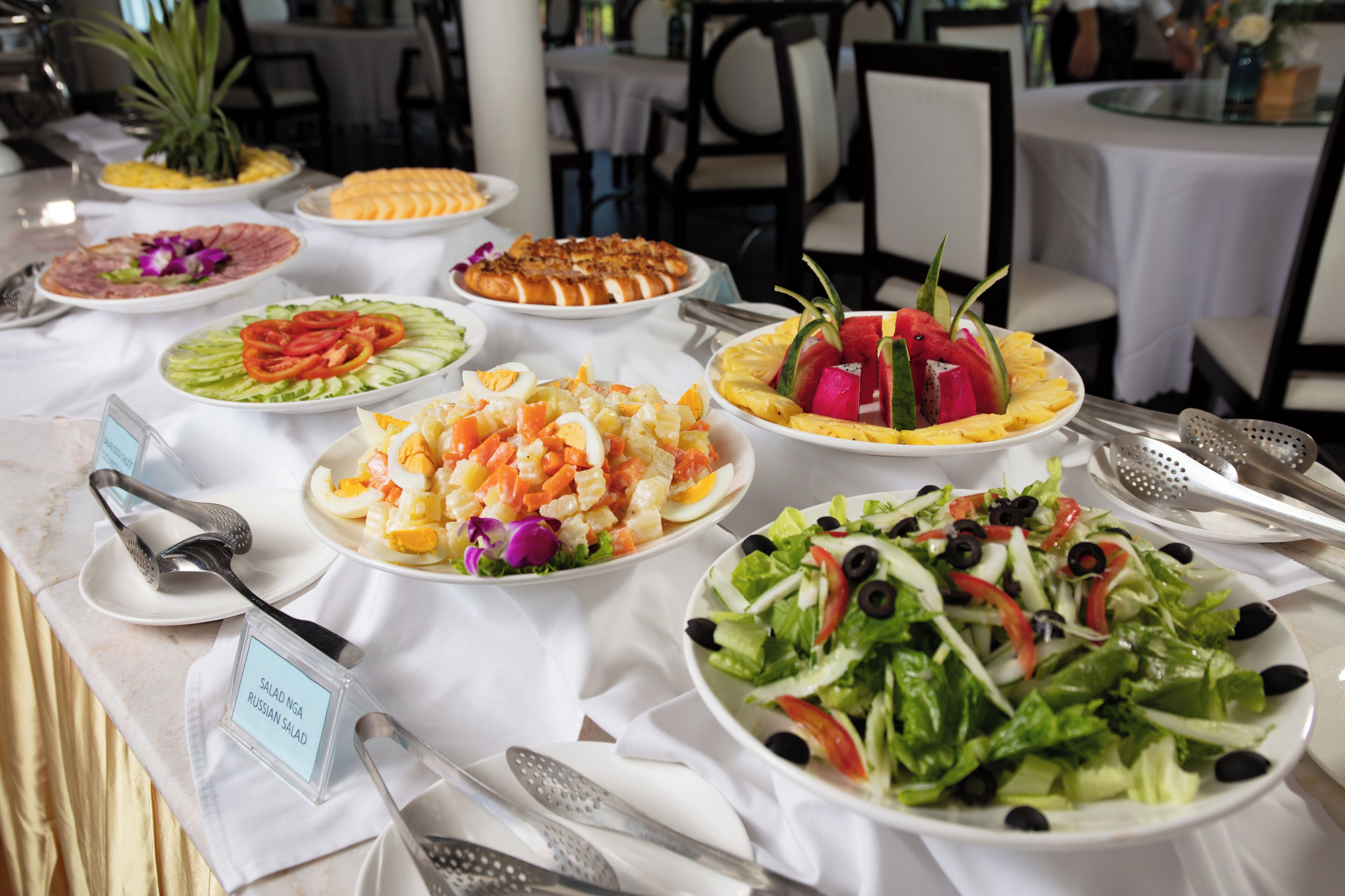 A buffet table with various dishes including salads, fruits, and a Russian salad.