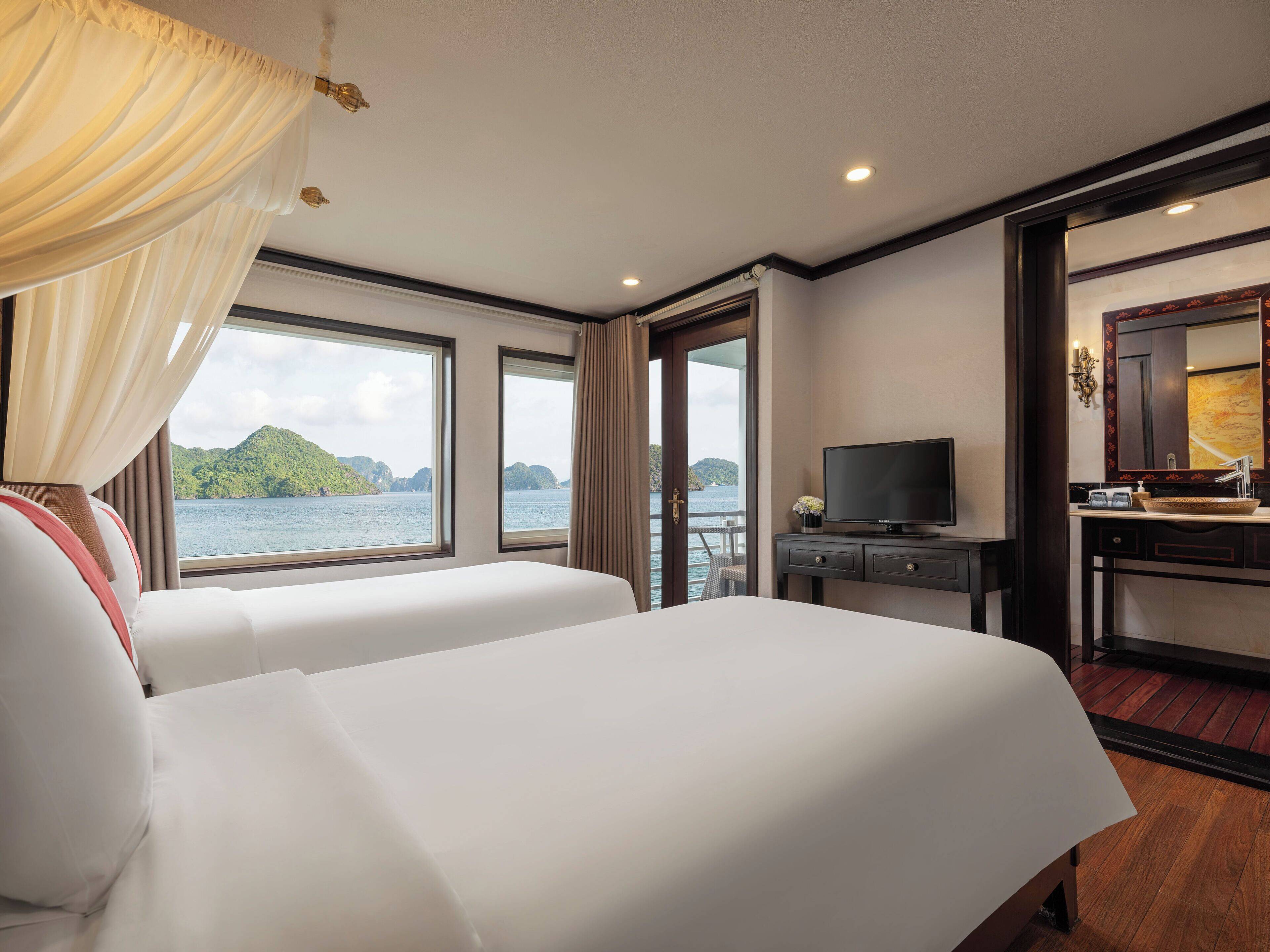 A hotel room with two beds, a TV, a desk, and a view of the sea.
