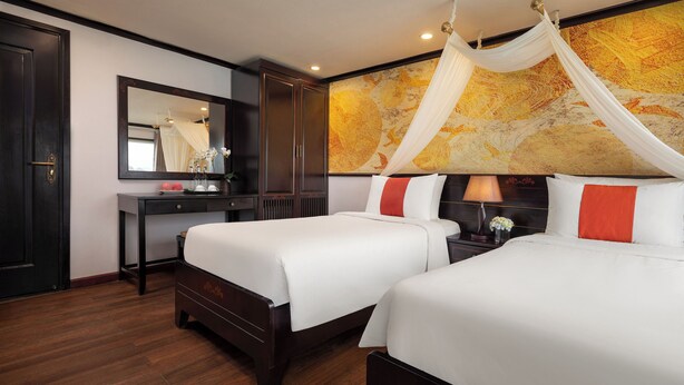 Quarto de hotel com duas camas, uma mesinha de cabeceira, um espelho e uma cama com dossel.