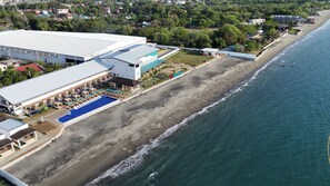 An aerial view of a coastal hotel with a swimming pool, beach access, and a large building with multiple balconies. - Hudor Resort (Bauang)