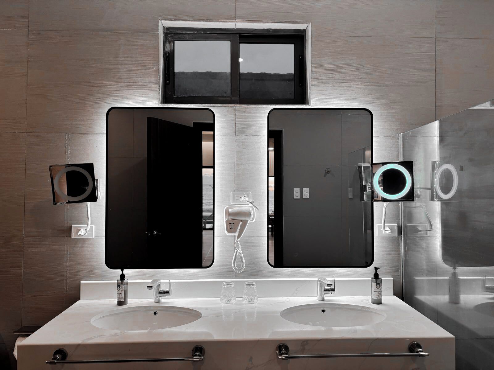 Un baño moderno con dos lavabos, un espejo grande y una ventana arriba.