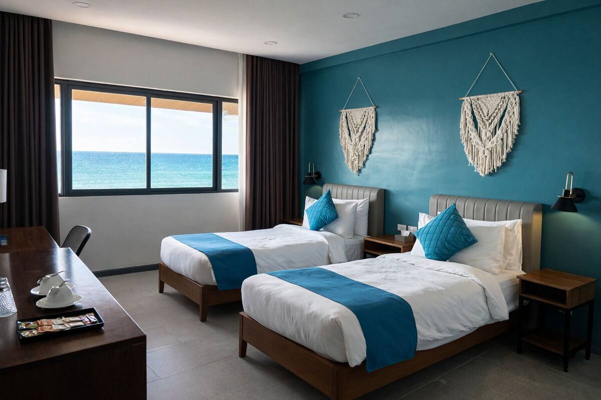 Camera d'albergo con due letti, una scrivania, vista sull'oceano e decorazioni macramè alle pareti.