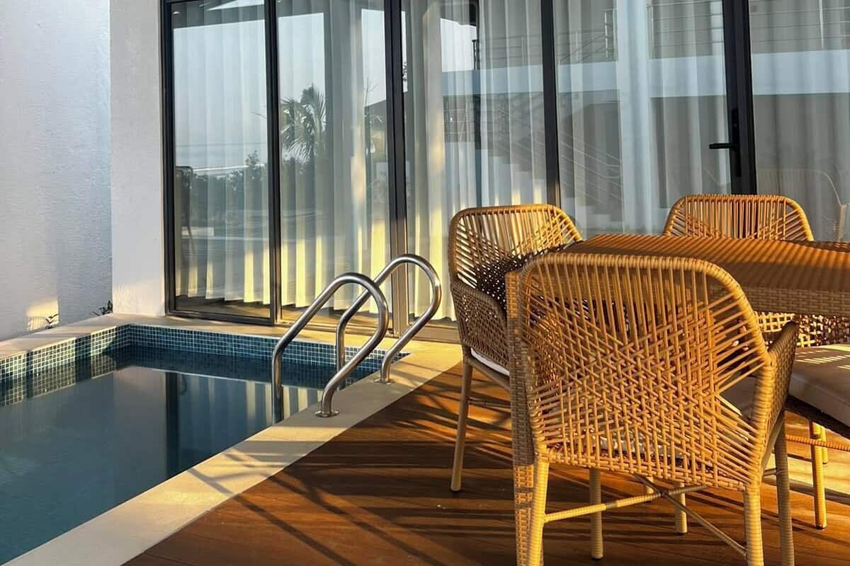 Area piscina interna moderna con soffitto in legno, ampie porte scorrevoli in vetro e mobili in vimini.
