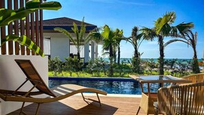 A poolside area with lounge chairs, a small table, and a view of a building and palm trees. - Hudor Resort (Bauang)