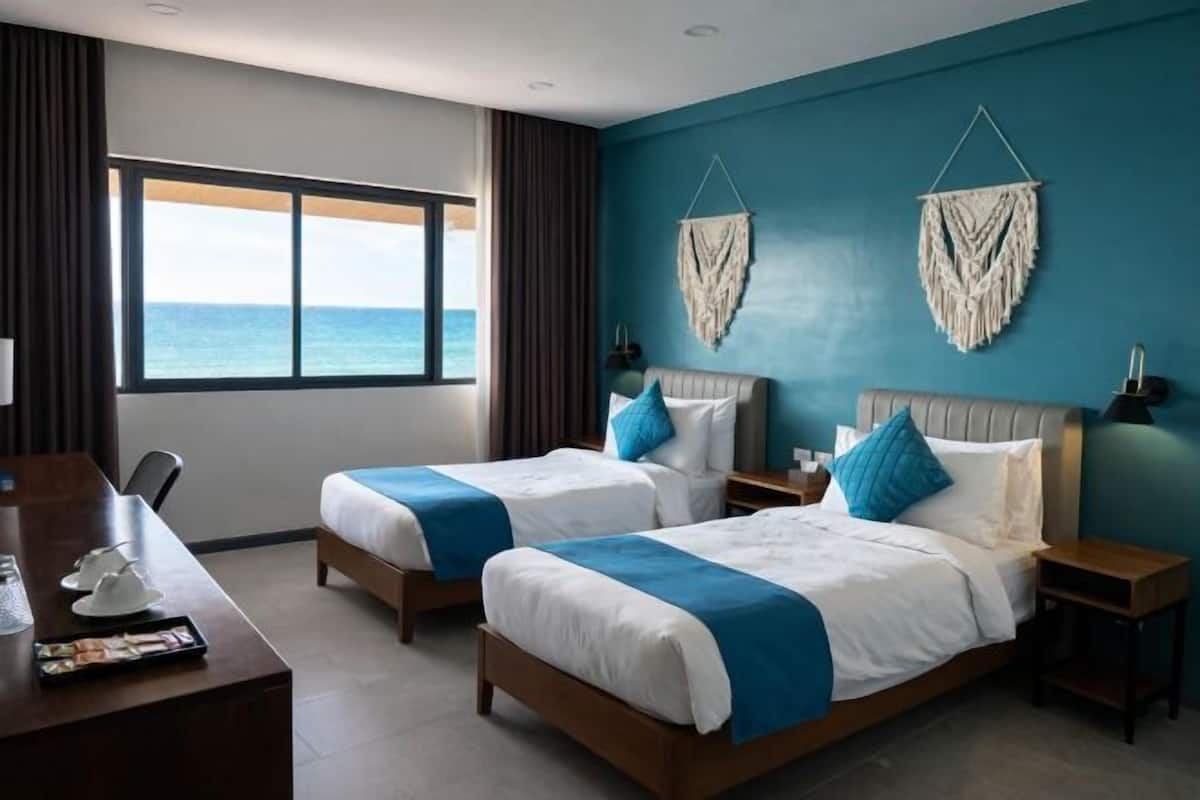 Camera d'albergo con due letti, una scrivania e vista sul mare.