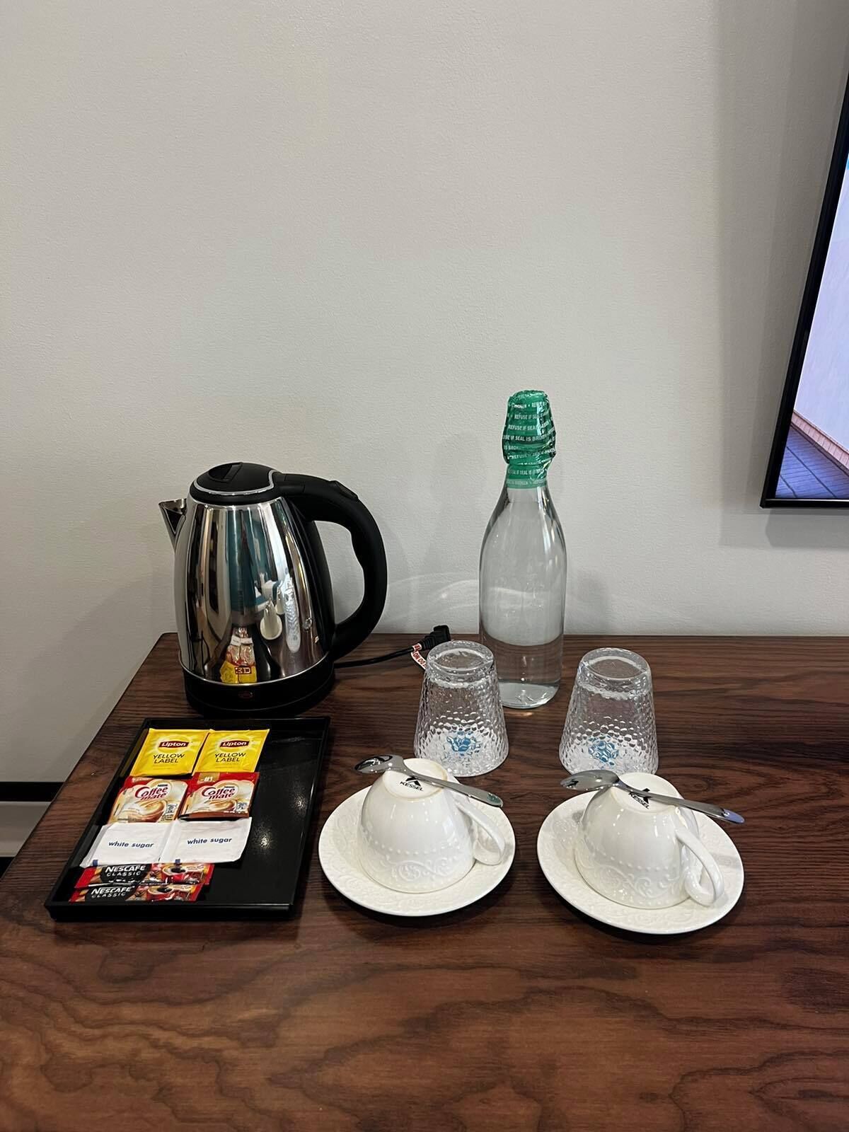 Una mesa con una tetera, una botella, dos tazas y una bandeja con sobres de café y azúcar.