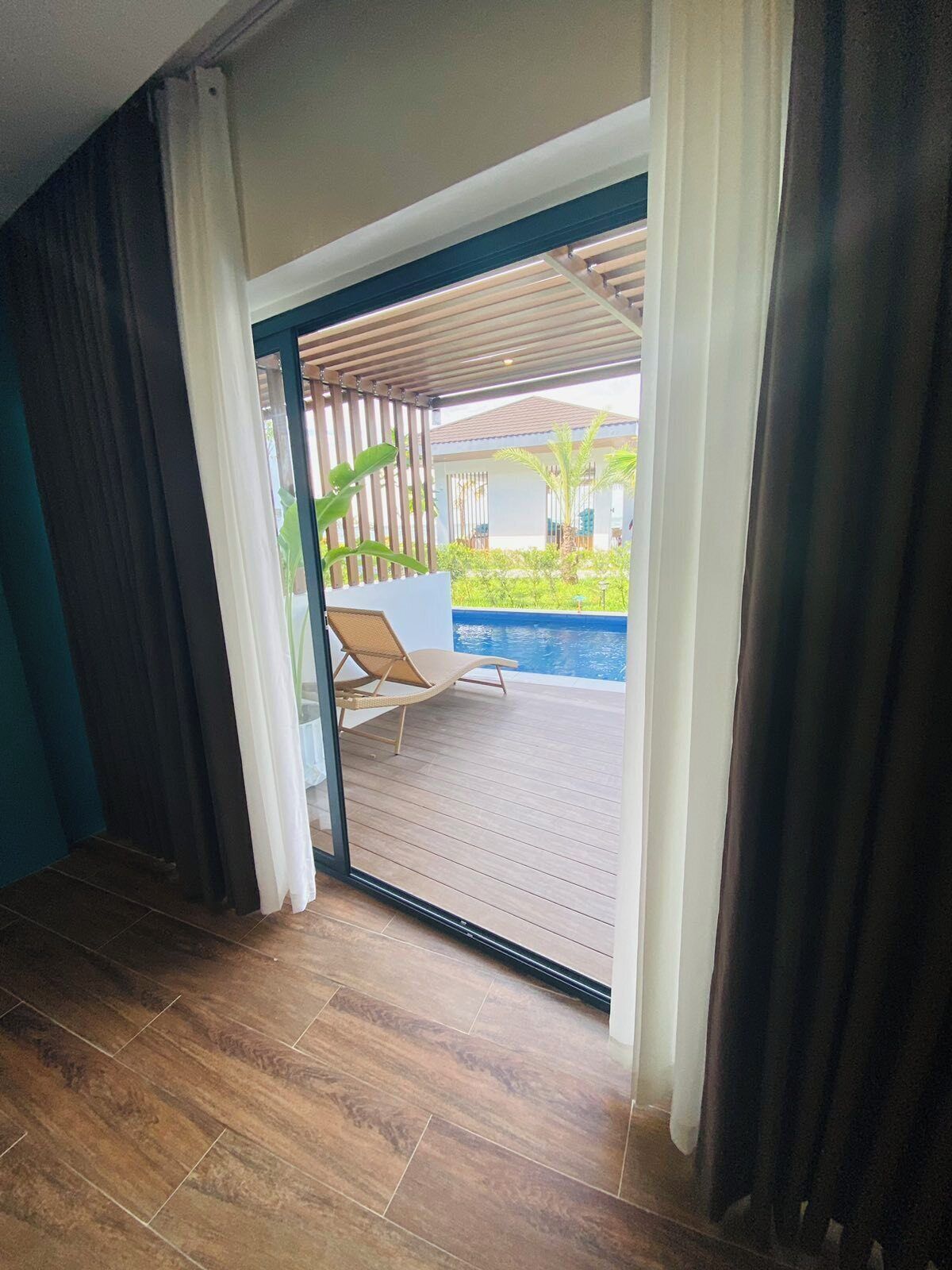 A room with a wooden floor, a sliding glass door leading to an outdoor area with a pool and lounge chairs.