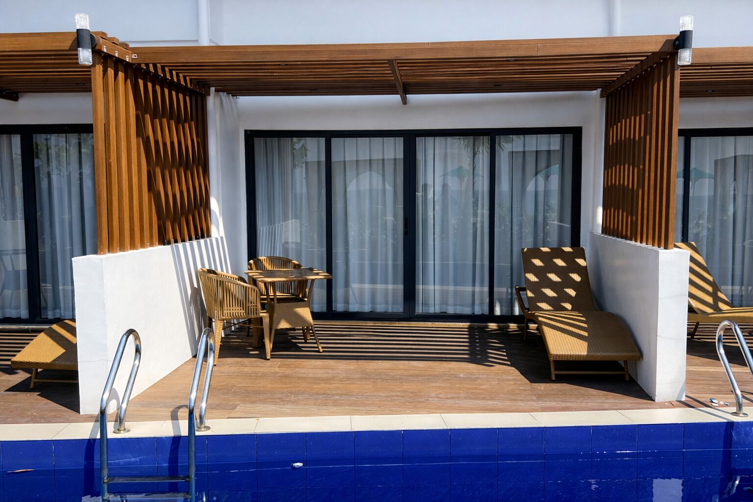A poolside area with a wooden deck, a table with chairs, and a lounge chair.