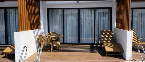 Un área junto a la piscina con maderas, una mesa con sillas y una tumbona.